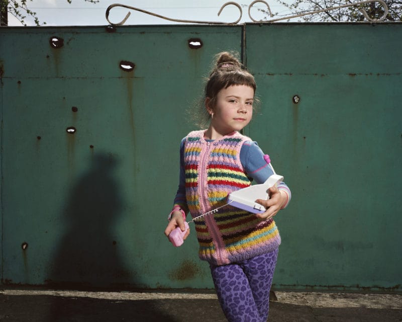 "An hour prior to these photographs being taken in September 2016, I had been sheltering with Kristina and her mother in the basement of their home in Troyitske, trying to escape the shelling. As soon as it stopped, Kristina insisted on going out to play in the garage, where she had set up a kind of impromptu theatrical stage with props."